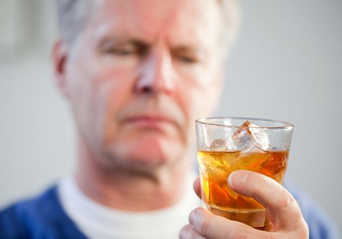 senior man looking at glass of whiskey