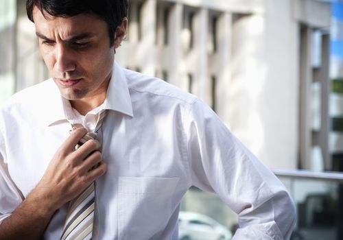 Hispanic businessman loosening necktie in office