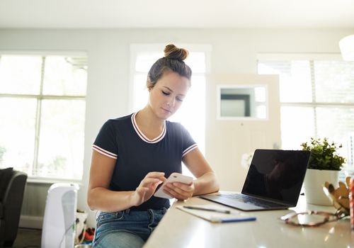 A young woman using a mobile phone while working at home