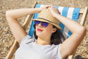 戴草帽和太阳镜的妇女晒日光浴在休息室椅子的海滩