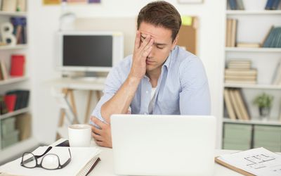 在笔记本电脑上工作的男人，揉着额头