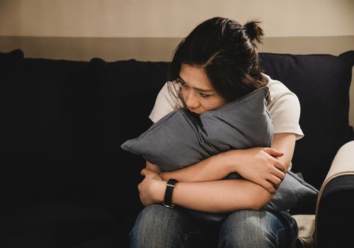 沮丧的亚洲女人坐在沙发上抱着一个垫子