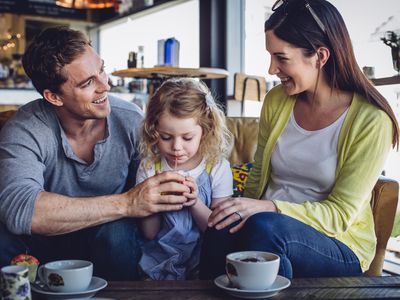 一对夫妇带着一个小女孩坐在咖啡店里享受着热饮和点心。