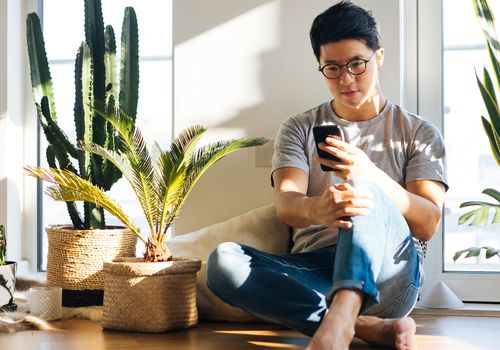 Young Man Using Smartphone At Home With Plants