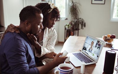 关闭咨询与他们的医生的一对年轻非洲夫妇在膝上型计算机的一个录影电话