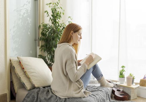 Woman with red hair writing in a journal on the bed.