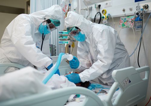 两位医生穿着头部脚趾保护装置在重症监护室内插管Covid-19患者。