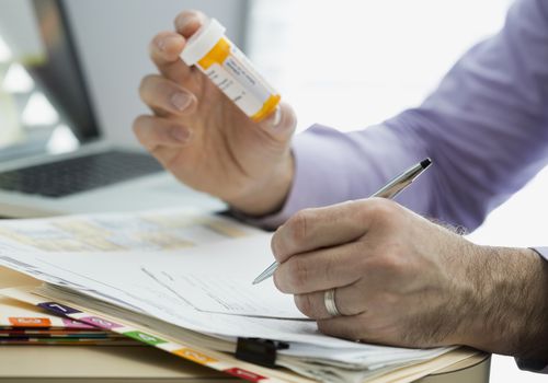 doctor writing prescription for medication with pill bottle in hand