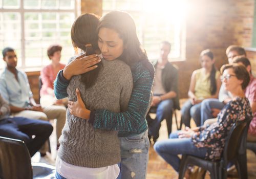 Two women hugging in a support group meeting