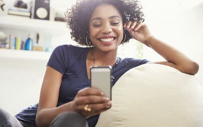 客厅沙发上，微笑的非洲裔妇女发短信用的手机