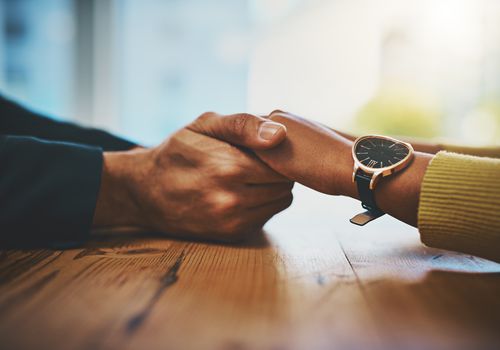 Cropped shot of a man and woman compassionately holding hands at a table