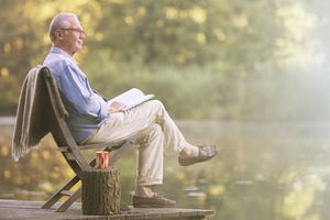 Older man reading book on dock at lake