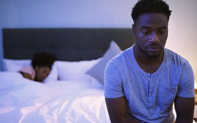 悲伤的男人坐在床边，而女人的伴侣正在睡觉
