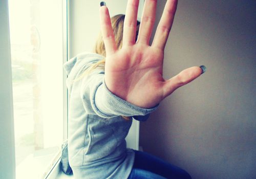 Woman sitting on window sill holding her hand up to the camera to block her face