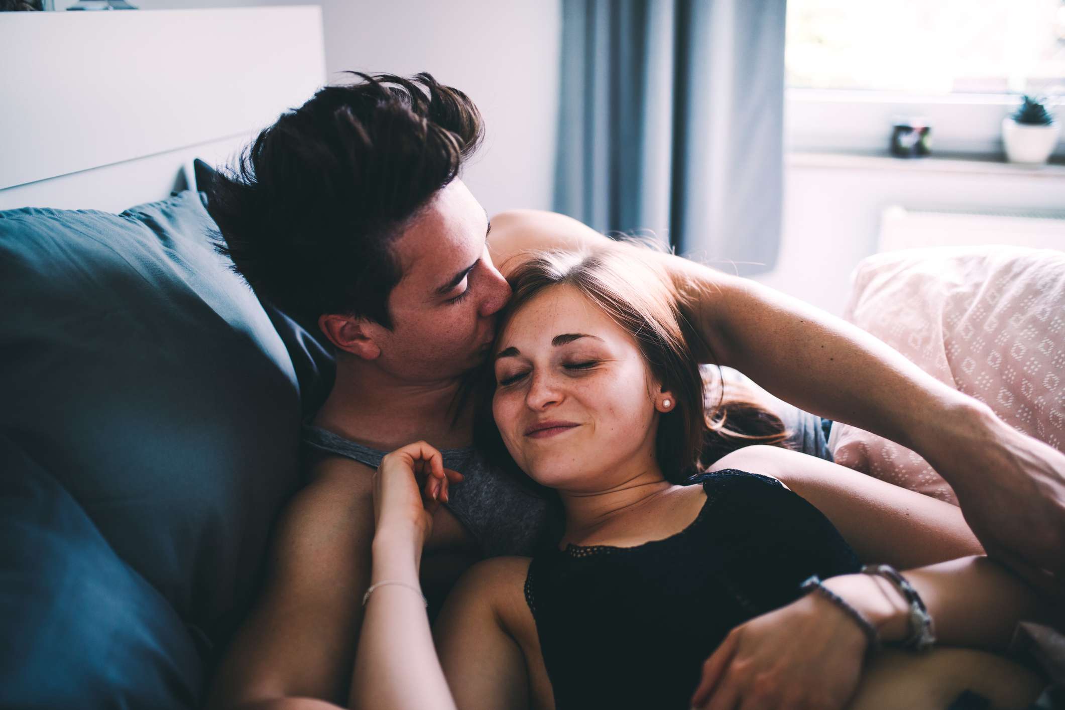Young man kissing a woman's forehead in bed