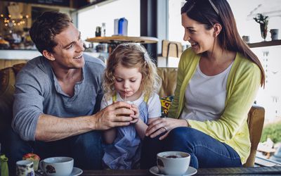 一对夫妇与一个小女孩坐在一家咖啡店享受热饮和茶点。