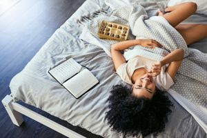 Bipoc妇女在床上与巧克力和期刊