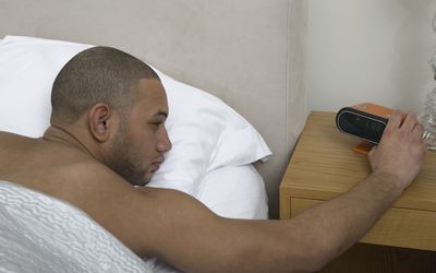 推挤在闹钟的年轻人贪睡按钮