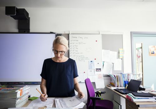 Teacher examining papers against blank whiteboard in classroom