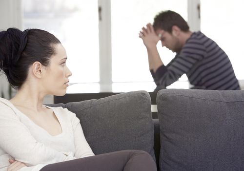 Young woman sitting on sofa, looking at distressed man at table