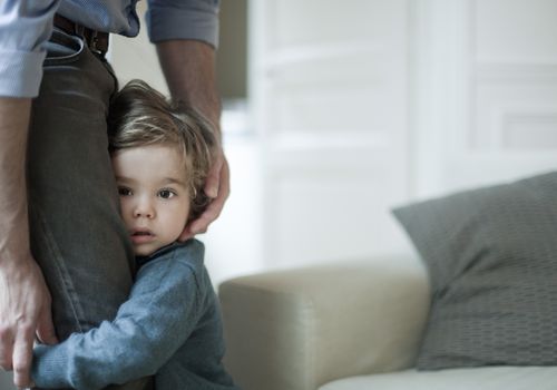 shy toddler boy holding into dad's legs