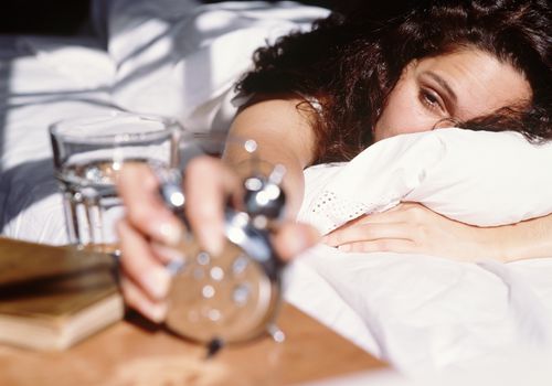 Woman lying in bed, turning off alarm clock