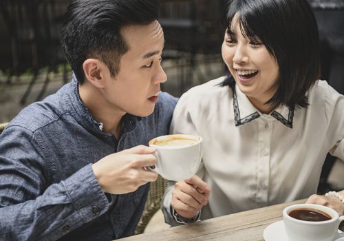 Chinese woman laughing at boyfriend with coffee froth on lip