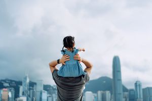 给小女儿肩扛乘坐的年轻亚裔父亲背面图由散步