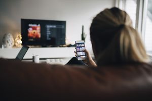 使用智能手机的少妇的脑袋在看电视时。