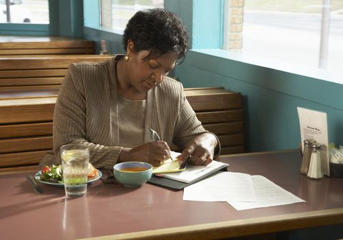 Woman sitting at table in diner writing on paper