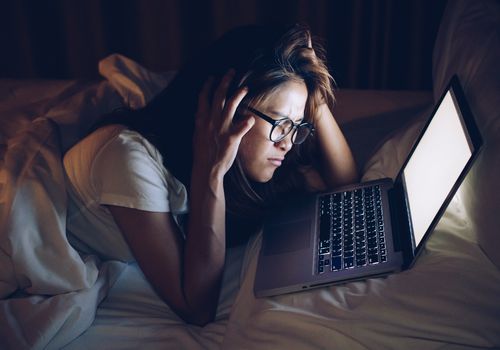 Distressed young woman looking at laptop in bed in the dark