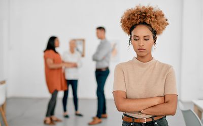 一个棕色卷发的女人站在那里，双臂交叉，远离三个模糊的人。