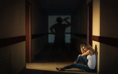 一个女人坐在走廊里，一个男人在影子里喝酒