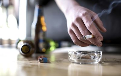 一个拿着香烟，地上放着啤酒瓶的男人