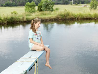 不开心的女孩坐在池塘边的跳板上