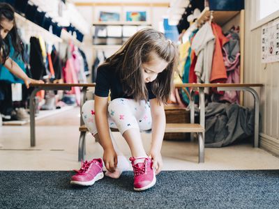 Full length of girl sitting on bench wearing shoes in cloakroom at preschool
