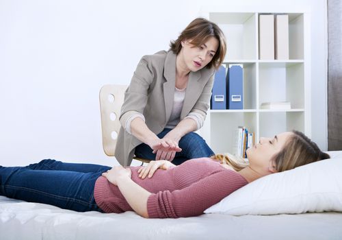 Therapist performing hypnotherapy on a woman lying down