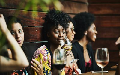 一个女人慢慢啜饮一杯酒在餐馆,被幸福包围的朋友。