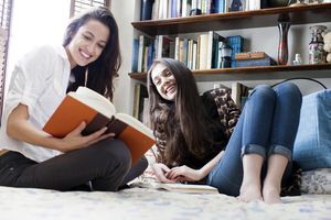 Two Girl Friends Reading In Bed And Laughing