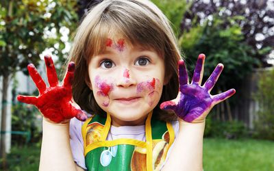 小女孩在她的手和脸油漆