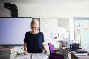 Teacher examining papers against blank whiteboard in classroom