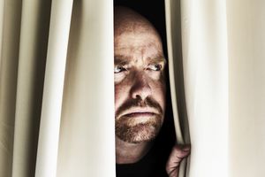 忧心忡忡的男人皱着眉头，透过紧闭的窗帘往外看