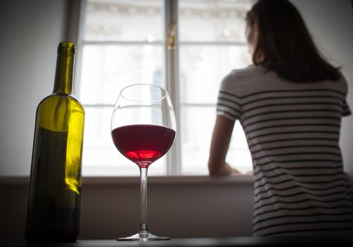 woman looking out window with glass of wine on table