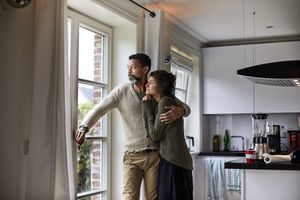 沉思的人盯着窗外周围的女人手臂“class=