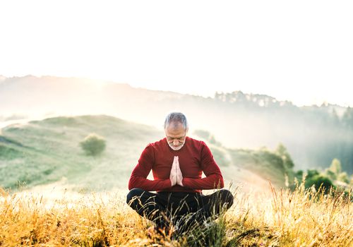Senior man meditating outdoors in nature in the foggy morning. Copy space.