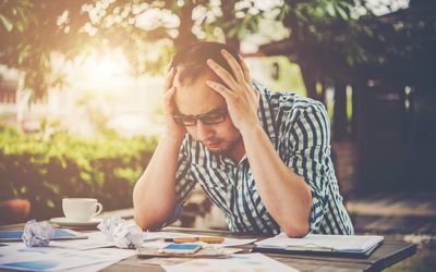 坐在书桌的沮丧的年轻人有头的在手上