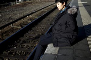 一名女子坐在火车站台上，双腿悬在边缘