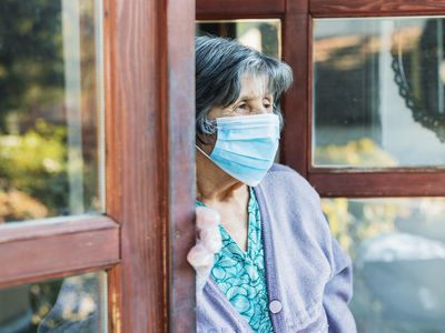 Older woman wearing mask stands alone