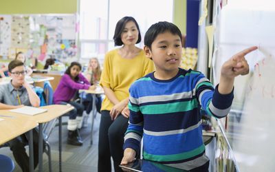 boy working with teacher on whiteboard in classroom