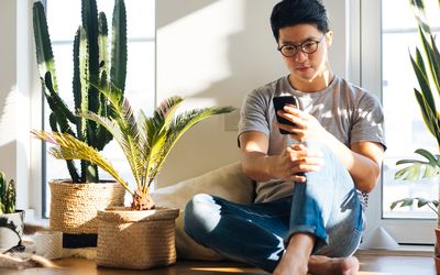 年轻男子在家里用智能手机和植物